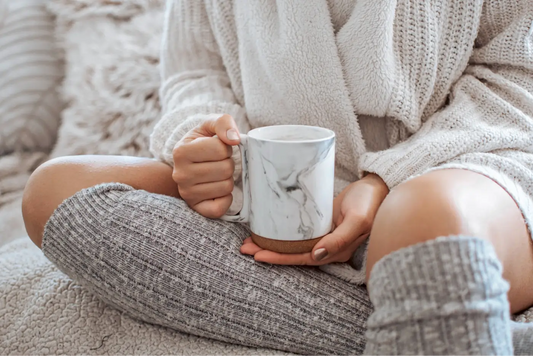 femme avec un plaid sur un canapé qui tient une tasse d'eau chaude le soir